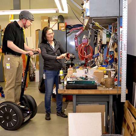 Foreman on Segway PT examing electrical component from female co-worker