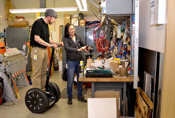 Foreman on Segway PT examing electrical component from female co-worker